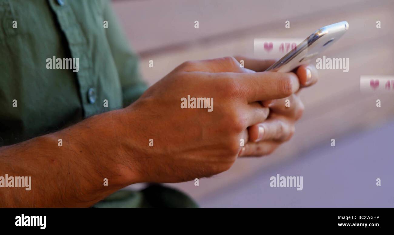 Uomo adulto con camicia verde che digita i messaggi su una panca di legno, con smartphone che riceve le notifiche Foto Stock