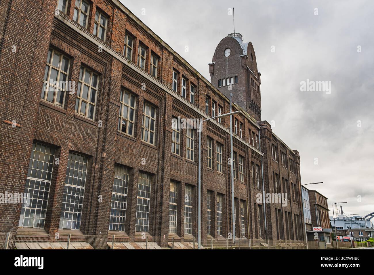 Uno storico edificio in mattoni in stile industriale con alte finestre e una torre dell'orologio nel quartiere Hafen di Düsseldorf, Germania Foto Stock
