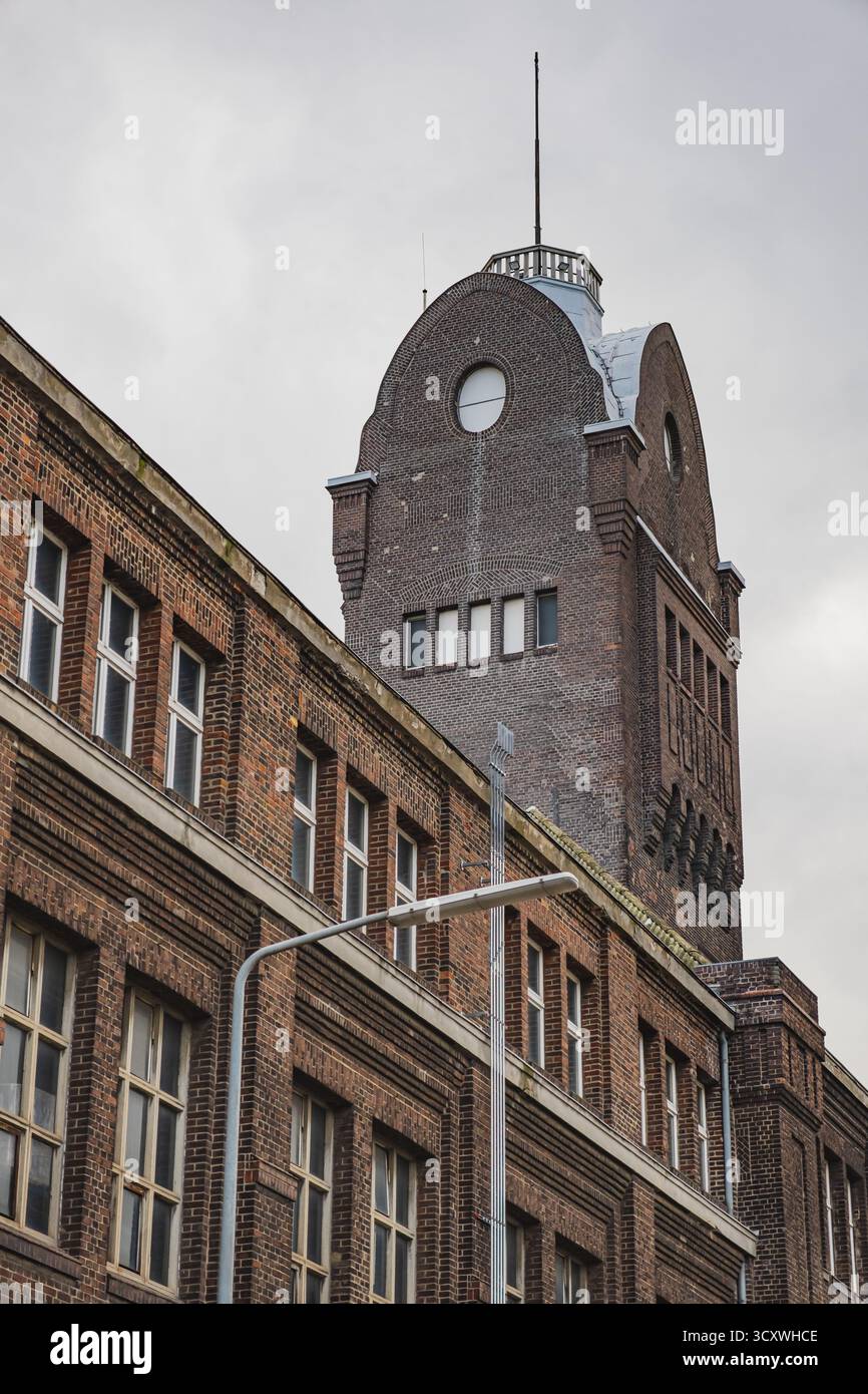 Uno storico edificio in mattoni in stile industriale con alte finestre e una torre dell'orologio nel quartiere Hafen di Düsseldorf, Germania Foto Stock