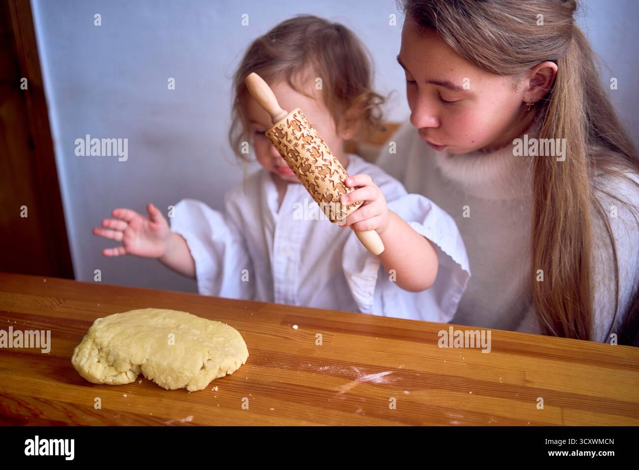 famiglia con due figlie, un adolescente e un bambino, cucinano biscotti insieme in cucina, amore da sorella Foto Stock