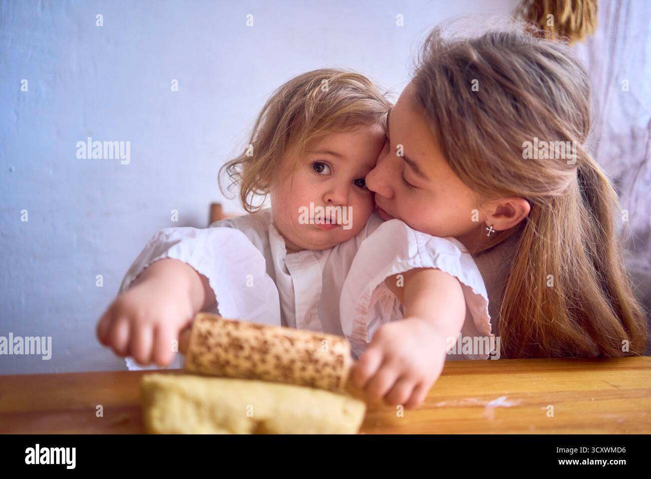 famiglia con due figlie, un adolescente e un bambino, cucinano biscotti insieme in cucina, amore da sorella Foto Stock