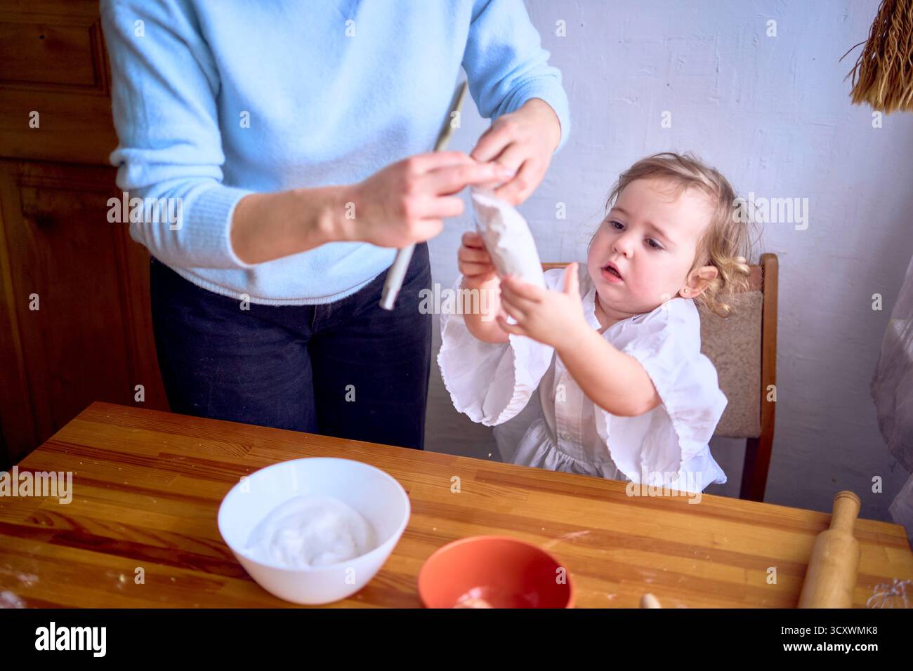 La mamma e un bimbo con il cranky cucinano la panna per una casa natalizia di pan di zenzero in cucina Foto Stock