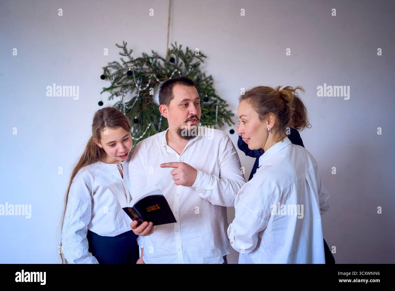 Famiglia con bambino e adolescente che legge la Bibbia durante le celebrazioni natalizie Foto Stock