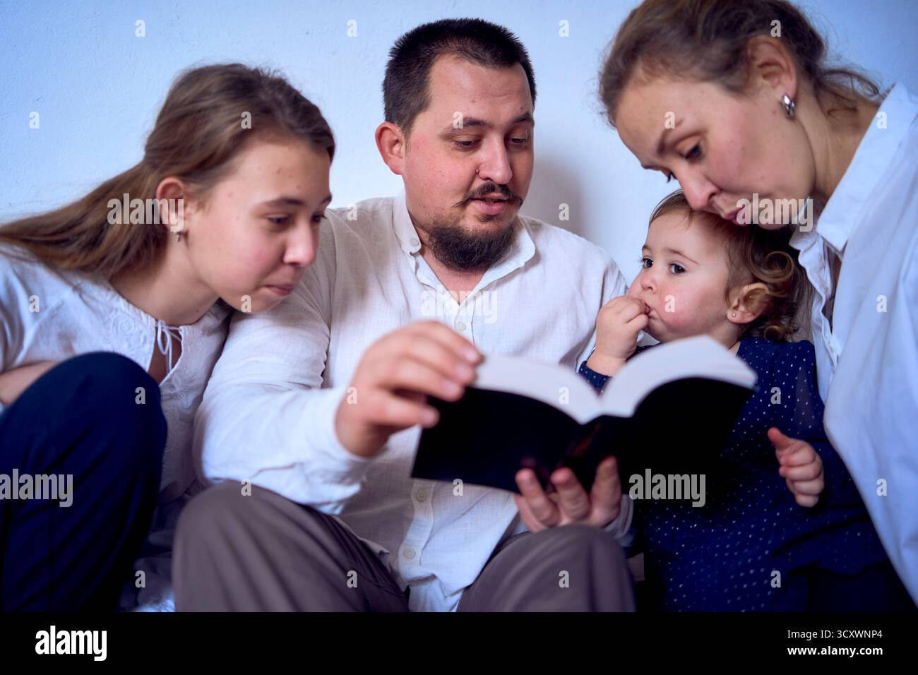 Famiglia con bambino e adolescente che legge la Bibbia durante le celebrazioni natalizie Foto Stock