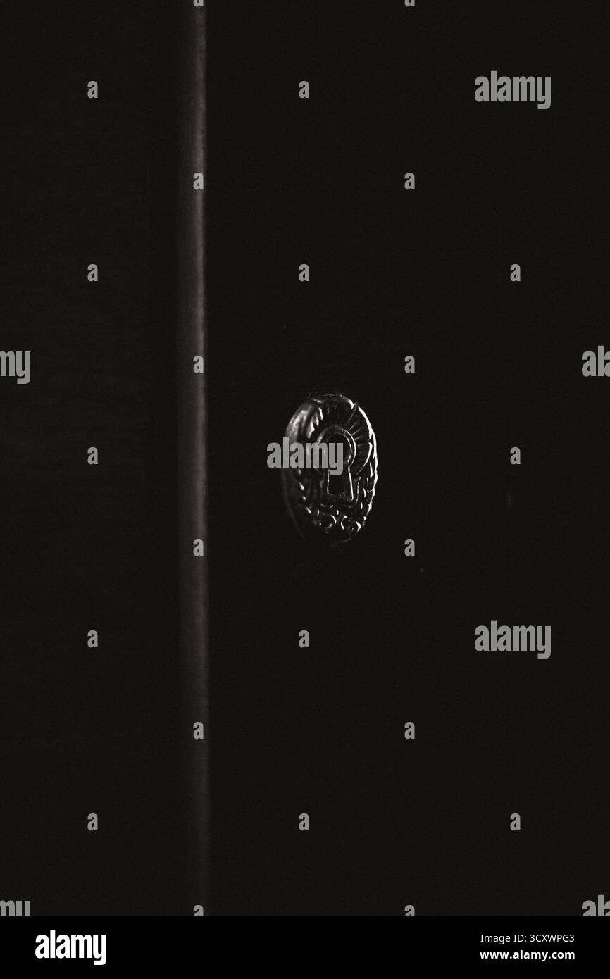 Primo piano di un'antica serratura su una porta di legno scuro. Atmosfera misteriosa e vintage con ombre profonde Foto Stock