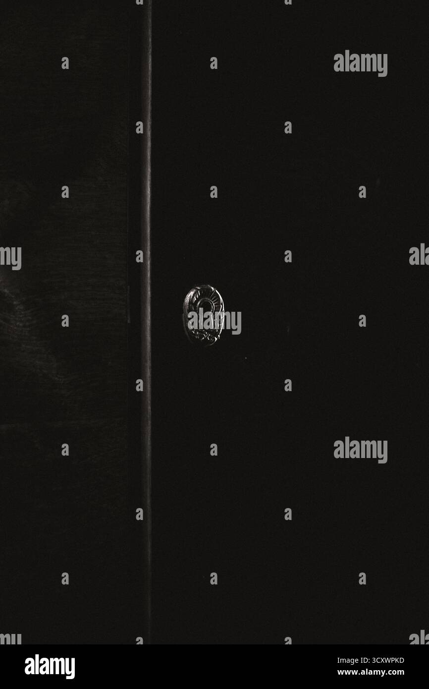 Primo piano di un'antica serratura su una porta di legno scuro. Atmosfera misteriosa e vintage con ombre profonde Foto Stock