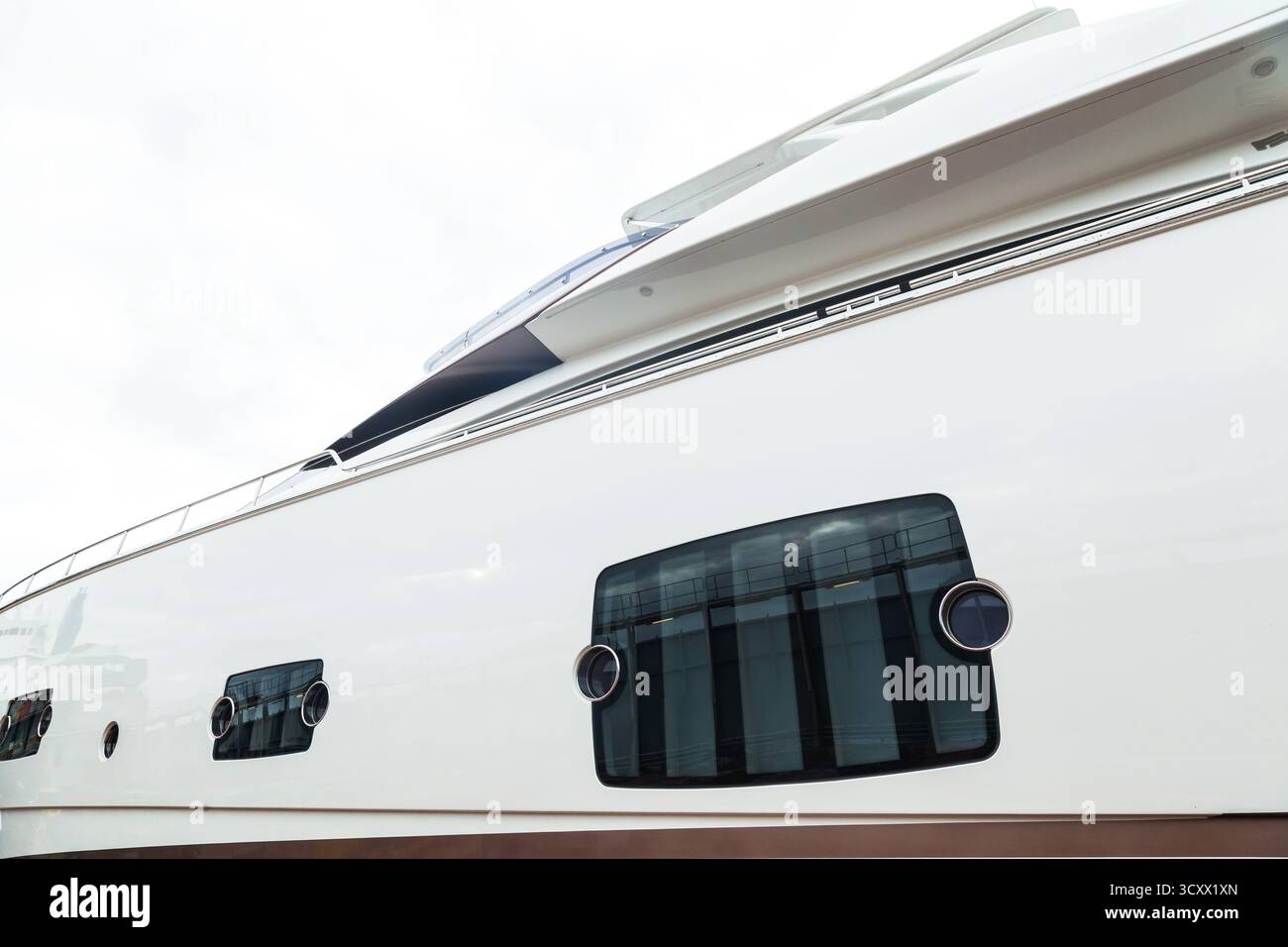 Vista laterale di un lussuoso yacht bianco motorizzato con oblò e corrimano, contro un cielo blu. Foto Stock