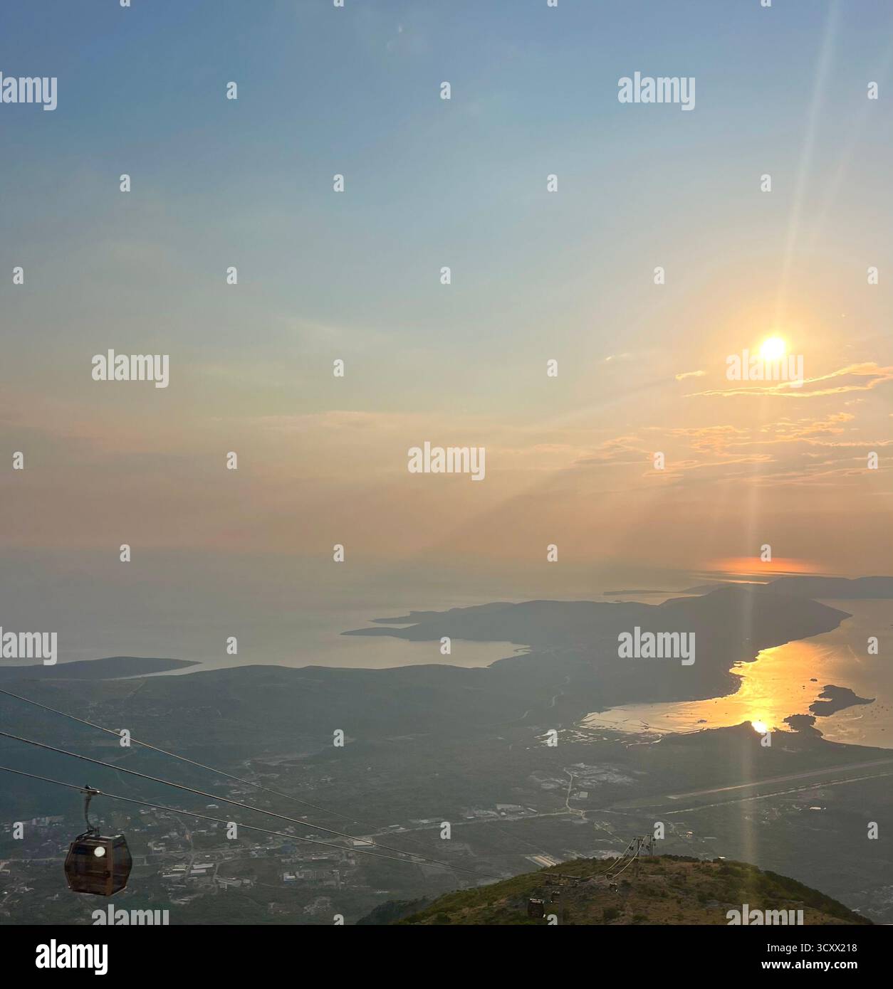 Vista del tramonto sul mare, che mostra una funivia che scende dalla montagna. La luce del sole dorata si riflette sul mare calmo, creando una scena tranquilla. - Immagine stock catturata con smartphone