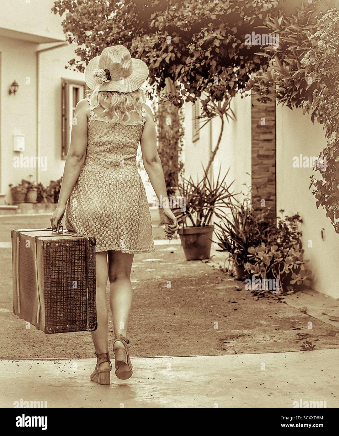 Donna in abito estivo e cappello che cammina con una valigia vintage. Foto Stock