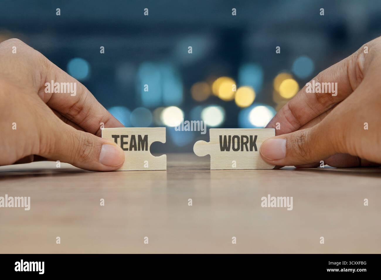Due mani che reggono pezzi di puzzle di legno con le parole SQUADRA e LAVORO. Lavoro di squadra, collaborazione, unità, partnership e concetto di cooperazione. Foto Stock