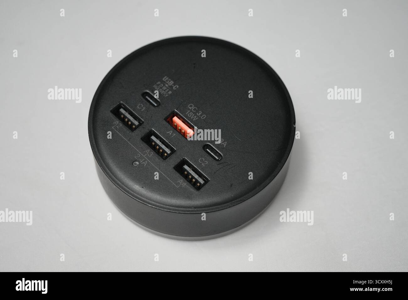 Londra, Regno Unito – 2025.10.16 – primo piano di un hub di ricarica USB circolare nero dotato di più porte USB-A e USB-C, tra cui QC 3,0 fast ch Foto Stock