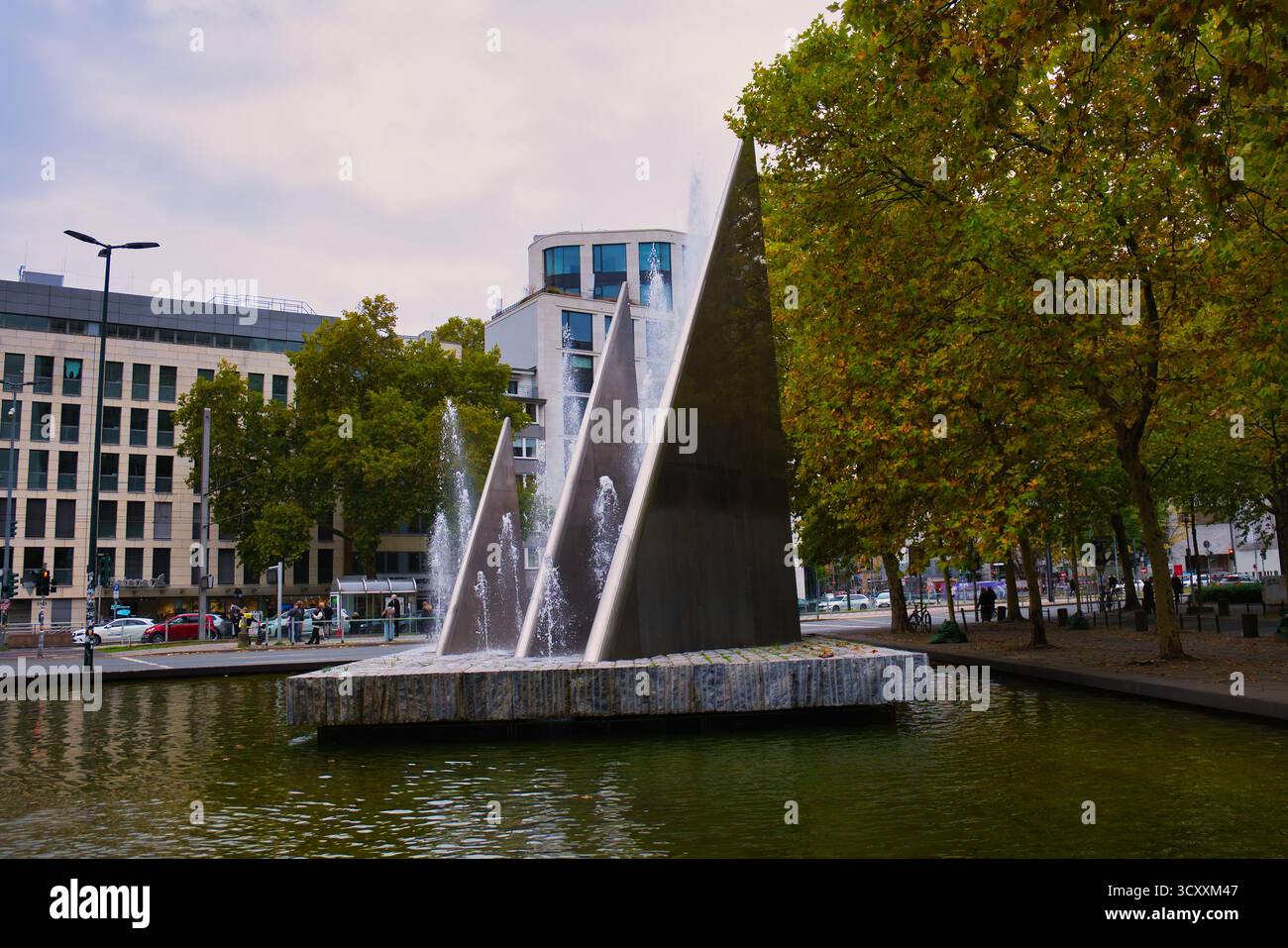 Fontana dinamica con sfondo architettonico moderno e vegetazione verde nel centro città Foto Stock