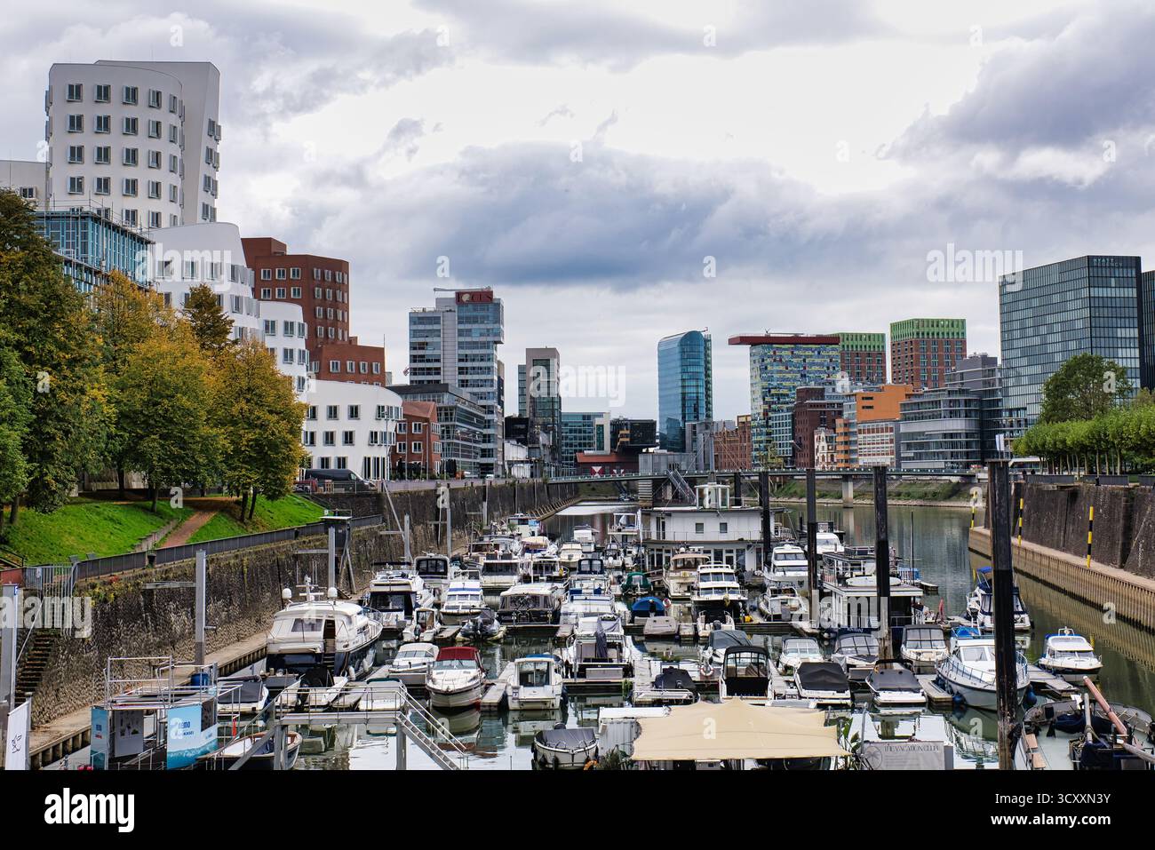 Gehry ha progettato edifici Twisted che si affacciano sulla trafficata Marina con barche attraccate e alberi d'autunno a Düsseldorf in Germania Foto Stock