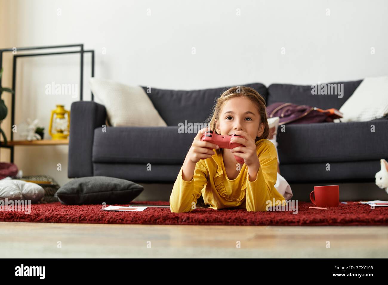 Una ragazza gioca ai videogiochi sul pavimento, circondata da cuscini e un'atmosfera accogliente a casa. Foto Stock
