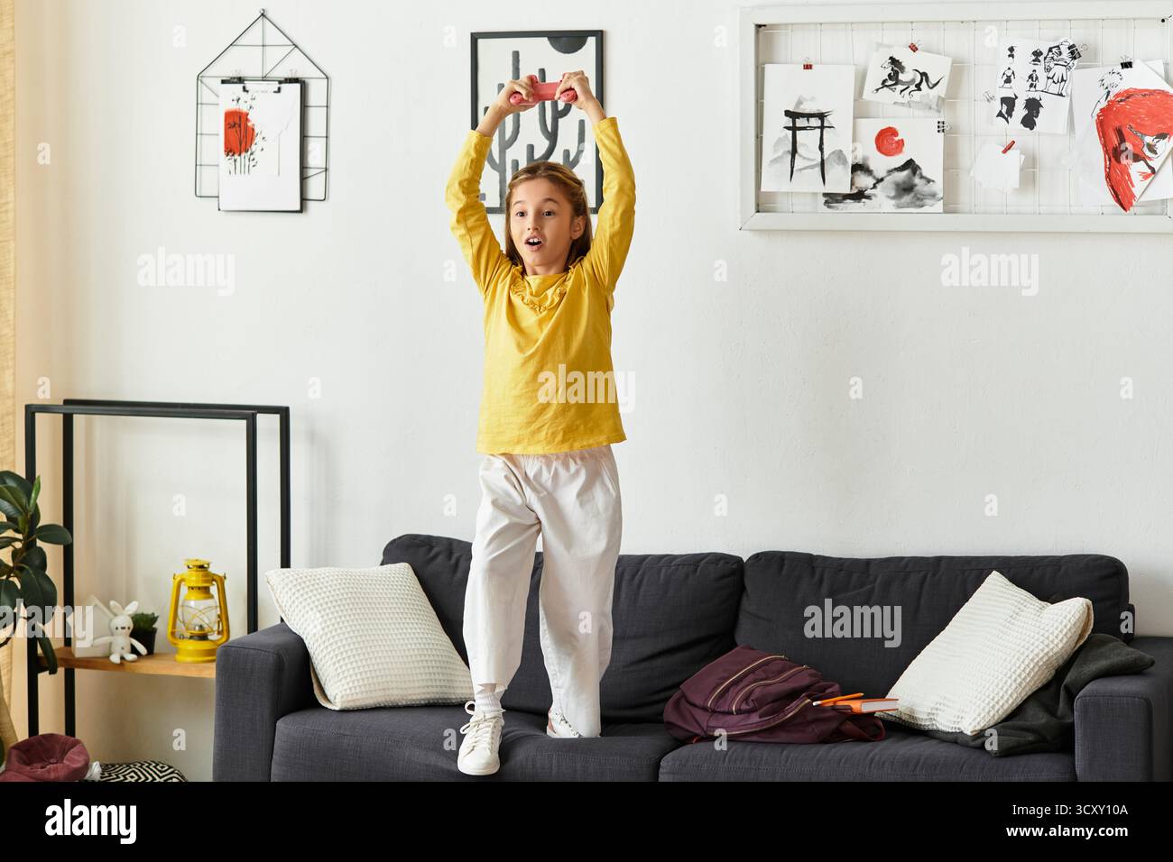 Una ragazza alfa gen esprime la sua felicità mentre gioca a casa, vestita comodamente e spensierata. Foto Stock