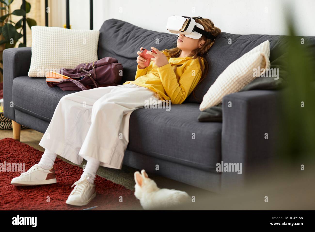 Una ragazza si rilassa sul divano, profondamente impegnata in un mondo di gioco virtuale mentre indossa una cuffia. Foto Stock