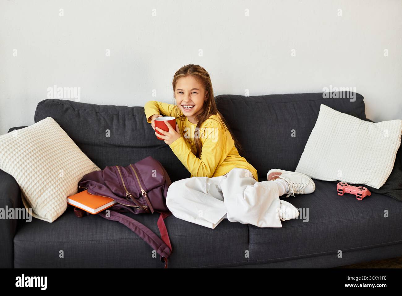 Una allegra ragazza alfa di generazione si rilassa sul divano, sorseggiando un drink mentre si diverte a casa. Foto Stock
