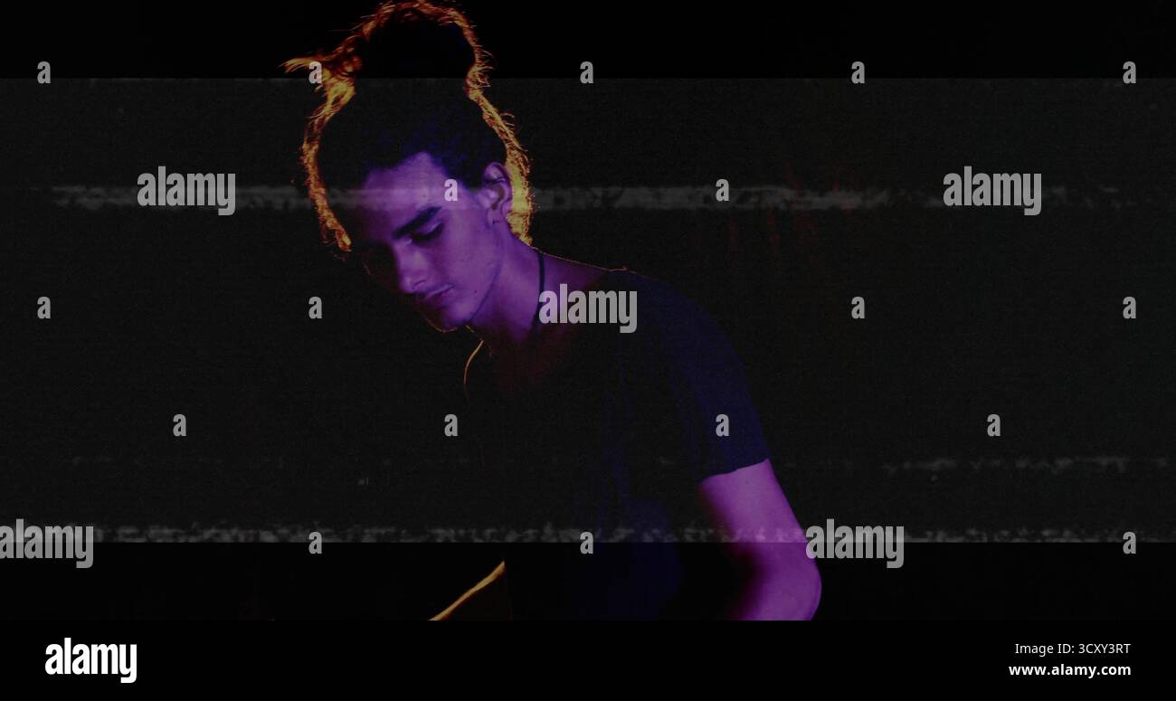 Esecutore maschile che regola i controlli audio in studio, con collana sottile e strisce luminose Foto Stock