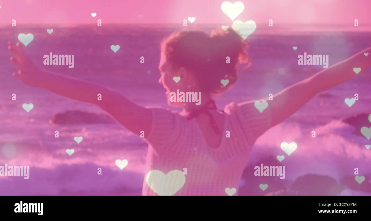 Donna che si allunga indossando la maglia che solleva le braccia verso le onde al tramonto sulla spiaggia, con sovrapposizioni cardiache Foto Stock