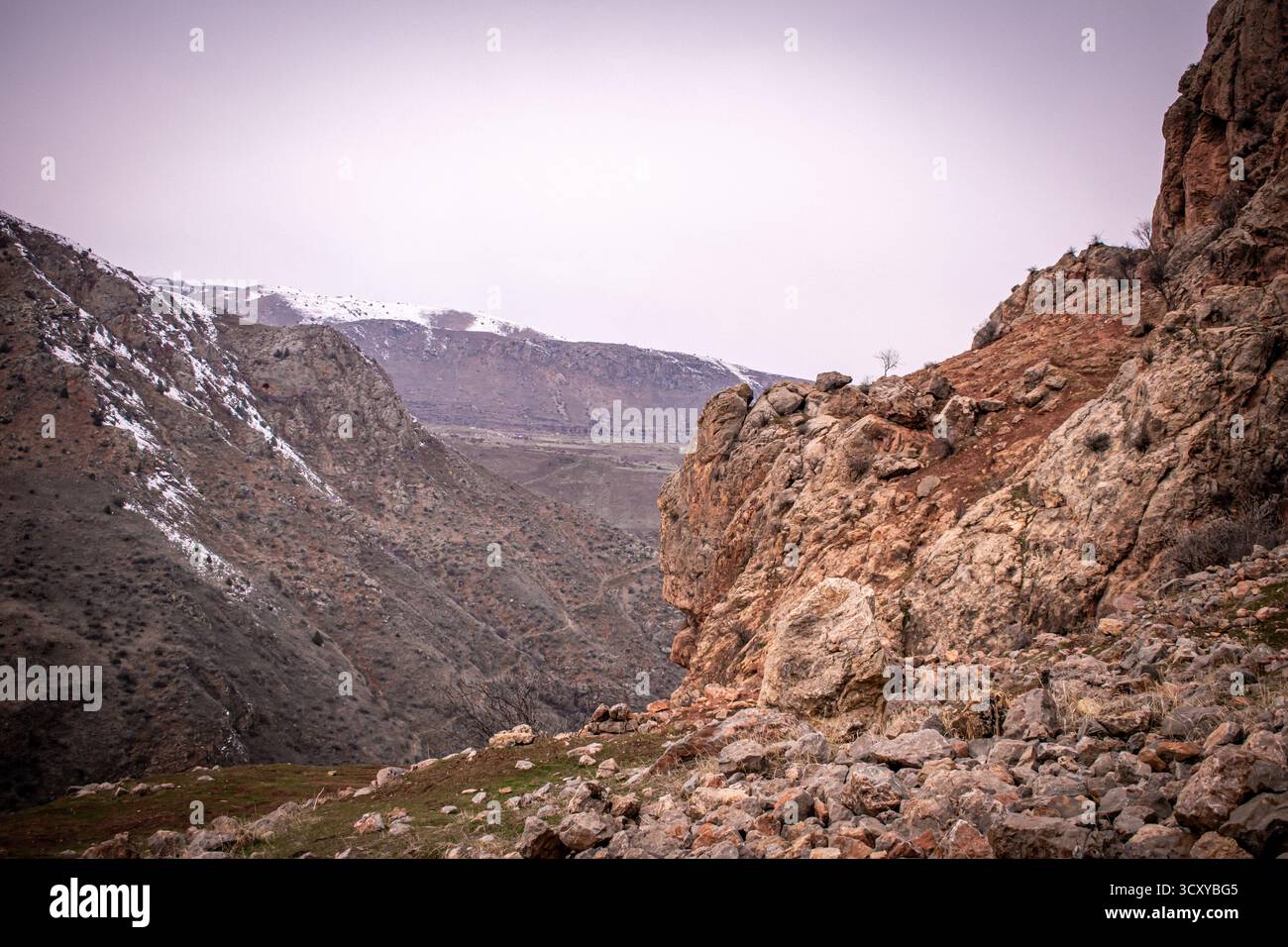 Un paesaggio montano in Armenia con aspre vette rossastre-arancioni che si estendono attraverso l'orizzonte. Alberi sparsi sono sparsi lungo i pendii. Foto Stock