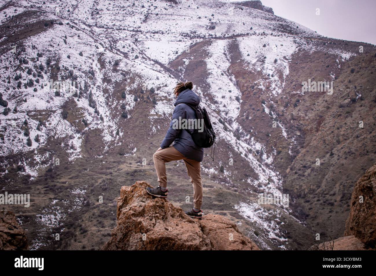 Montagne invernali dell'Armenia, le cui cime sono ricoperte di neve. Una persona con uno zaino sta in cima a una montagna. Foto Stock