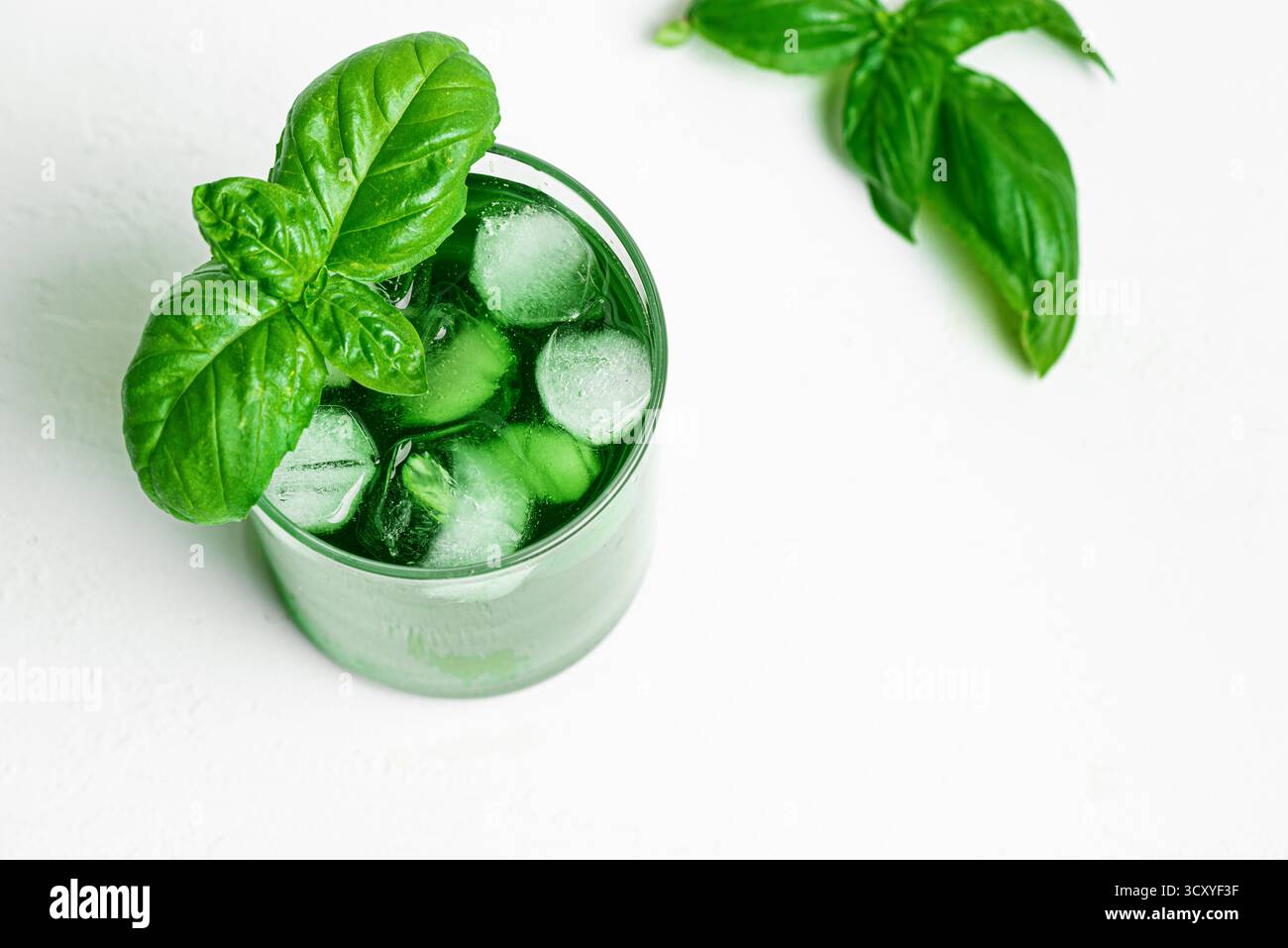 Bevanda liquida di clorofilla verde. Bicchiere di acqua di Chrorophyll con foglie di basilico su bianco, vista dall'alto, spazio copia. Mangiare sano, stile di vita pulito, disintossicarsi Foto Stock