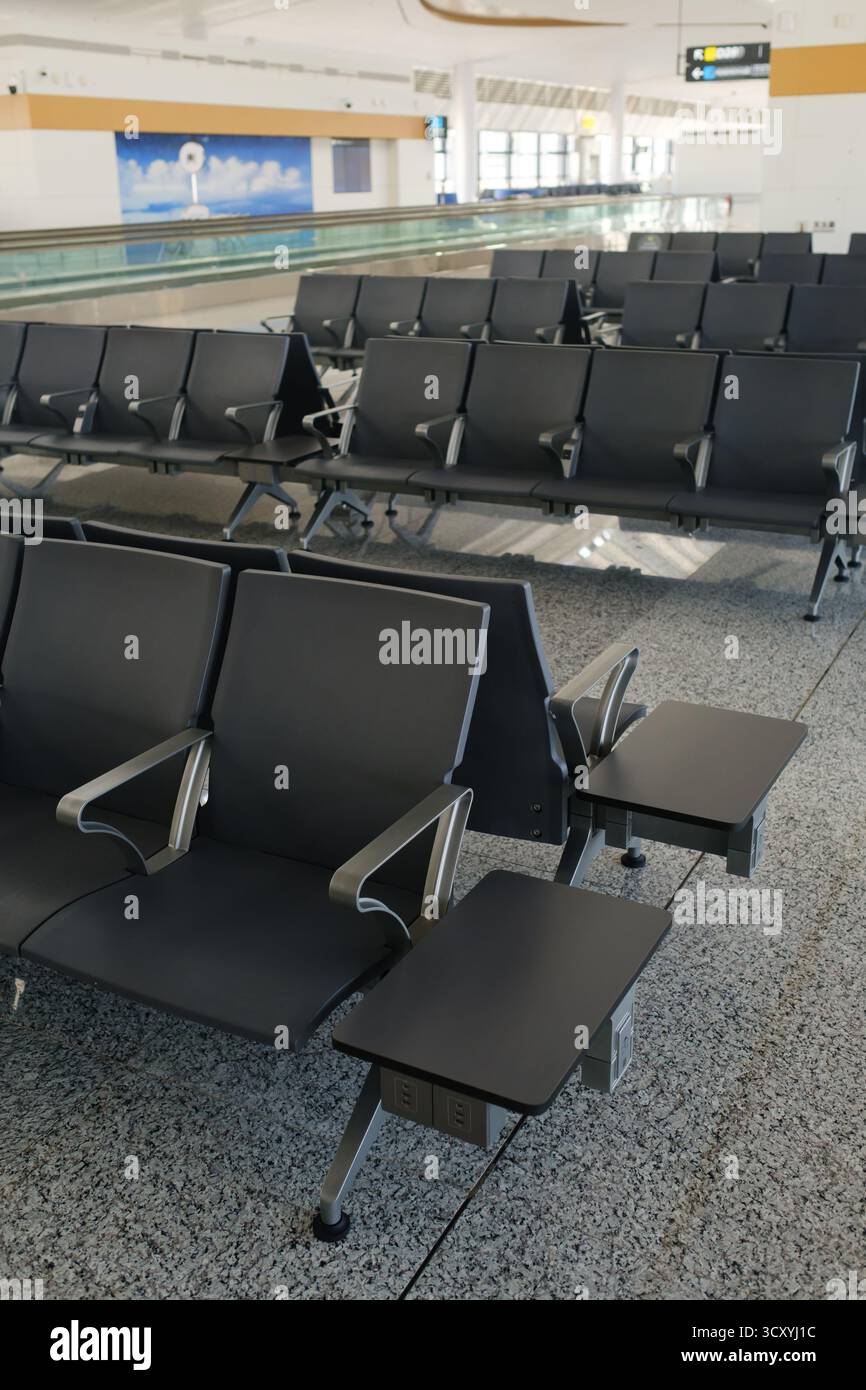 Il terminal aeroportuale abbandonato presenta file di eleganti posti a sedere neri con tavoli integrati. La luce naturale inonda lo spazio, mettendo in risalto una nuotata unica Foto Stock