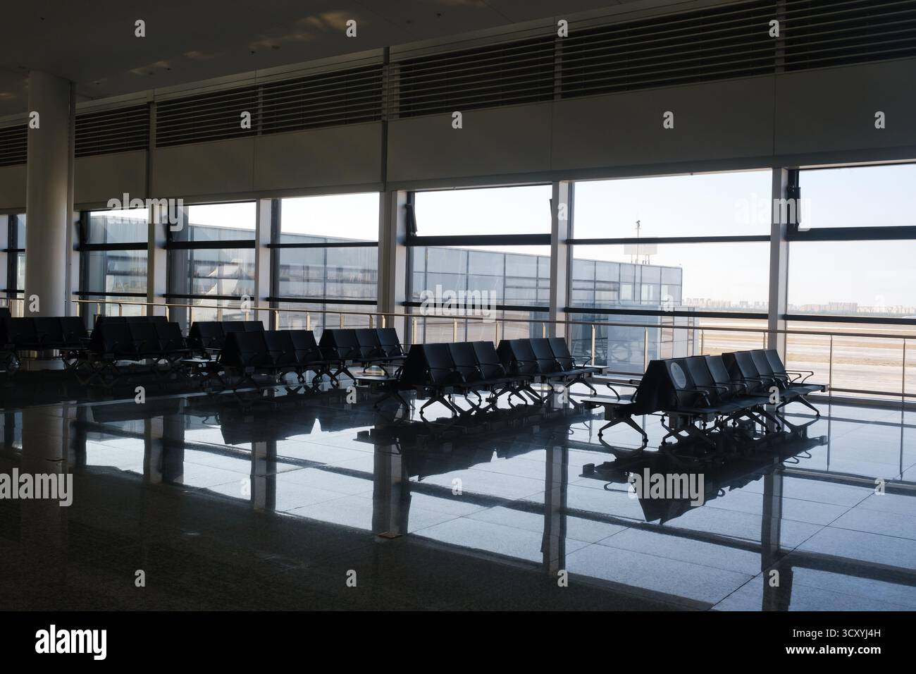 La luce del sole si riversa in un terminal aeroportuale vuoto, evidenziando file di posti a sedere disposti in modo ordinato. Le grandi finestre offrono una visuale chiara all'esterno, migliorando la qualità Foto Stock