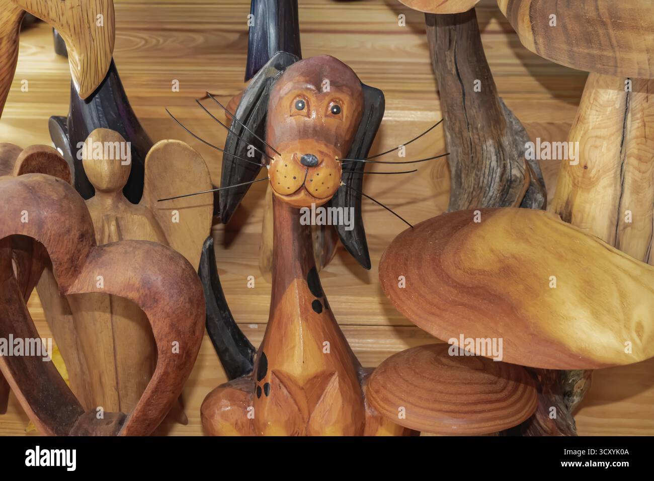 Affascinante figura di cane in legno fatta a mano con dettagli neri e un'espressione stravagante circondata da altre incisioni artigianali in legno, che riflettono la creatività, wa Foto Stock