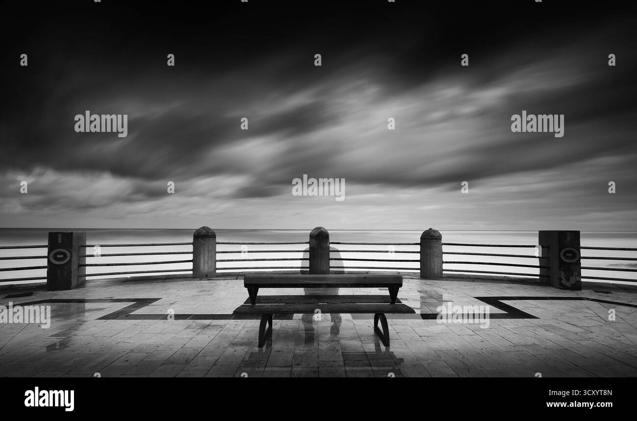 Una panchina e' seduta su un molo che si affaccia sull'oceano. Il cielo è nuvoloso e l'acqua è calma Foto Stock