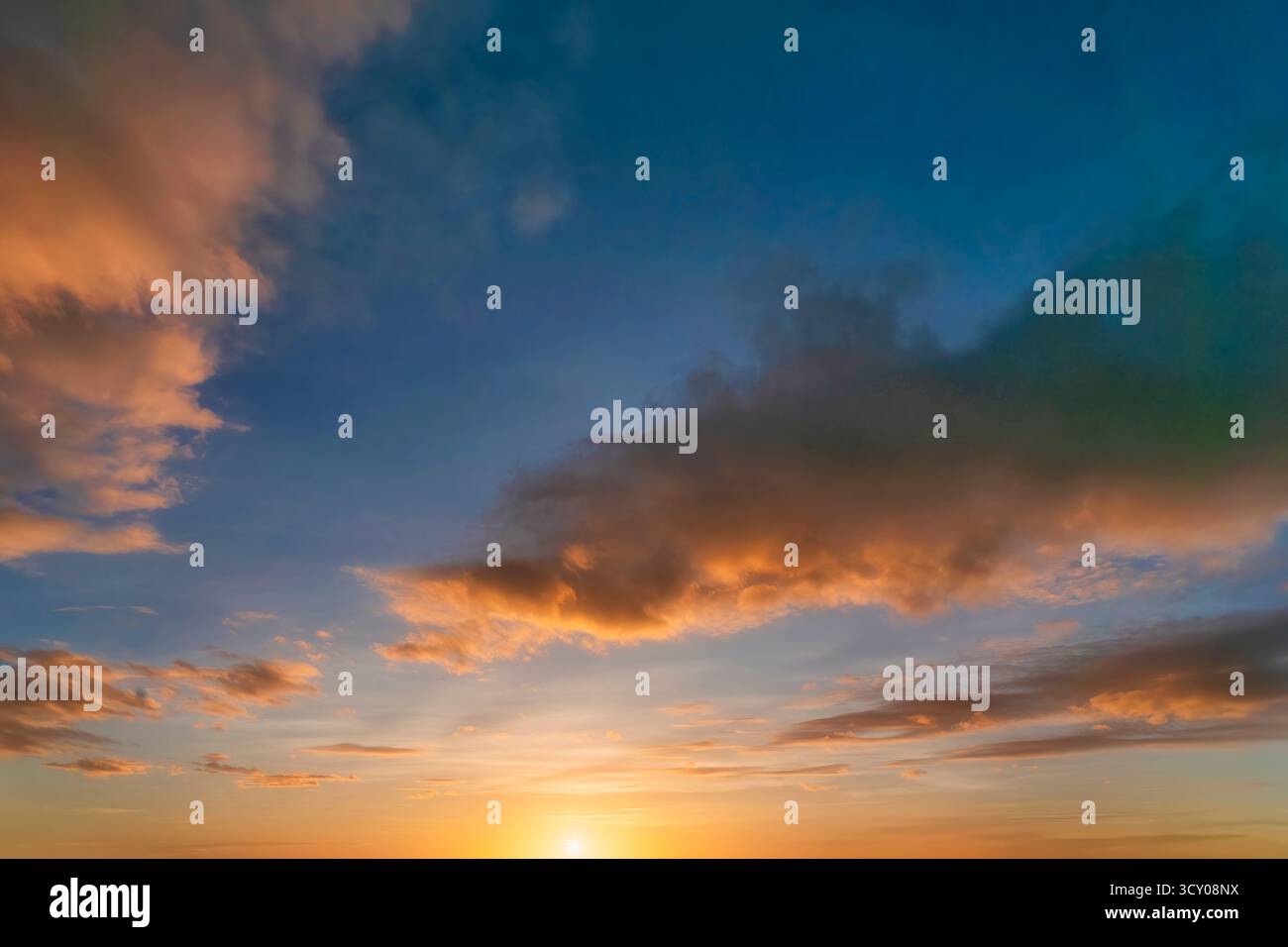 Cielo colorato e spettacolare al tramonto con nuvole arancioni, blu e grigie. Sfondo crepuscolare dell'ora d'oro con colori caldi e vivaci che sbiadiscono in sera Foto Stock