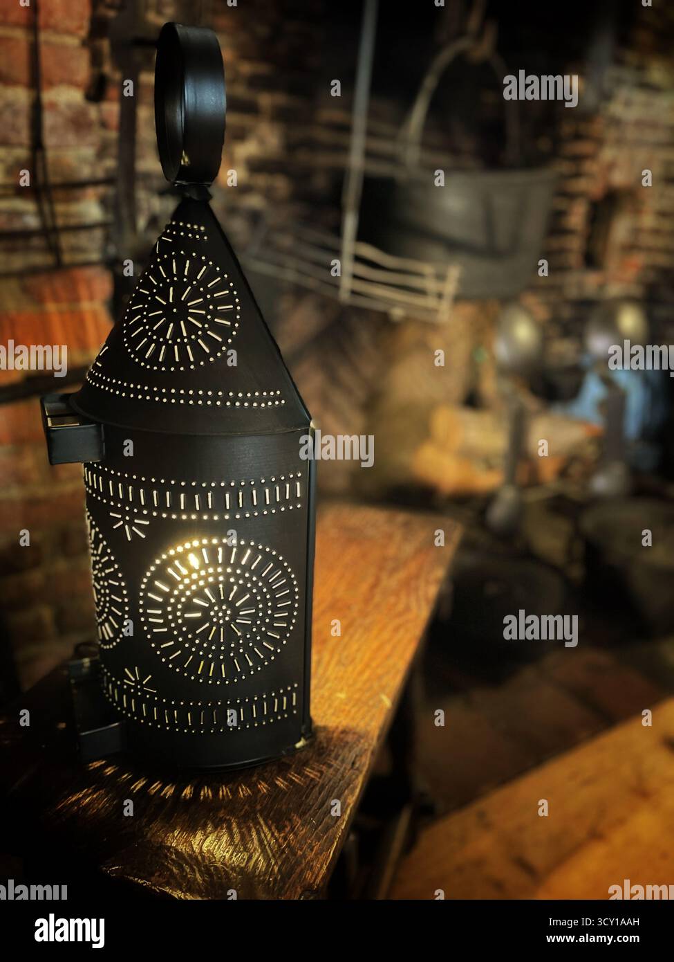Una lanterna in metallo vintage decorata con motivi intricati si illumina delicatamente nell'ambiente rustico di un laboratorio vecchio stile. Foto Stock