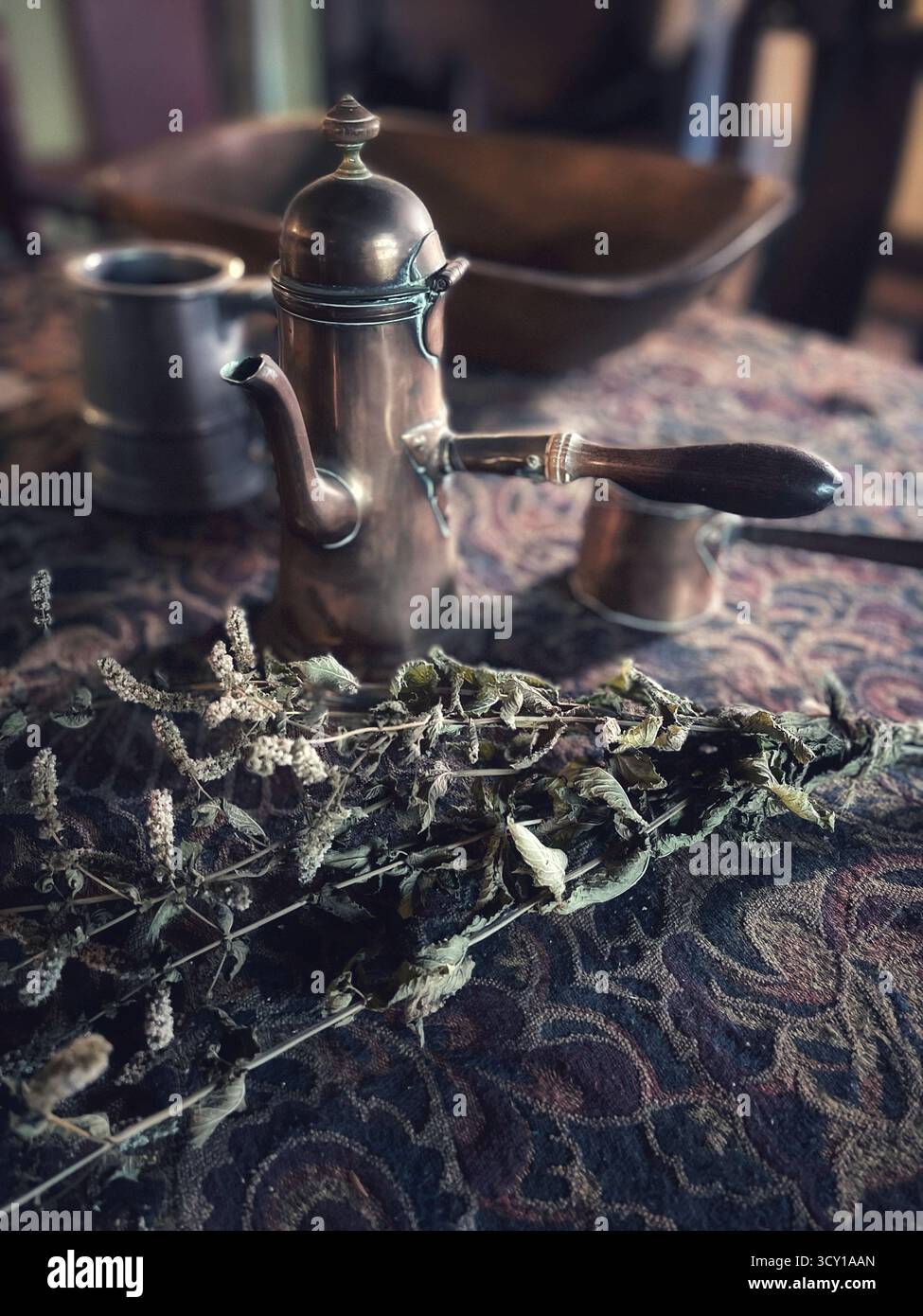 Caffettiera in metallo vintage e erbe essiccate su una tovaglia a motivi geometrici creano un'atmosfera nostalgica e rustica da cucina Foto Stock