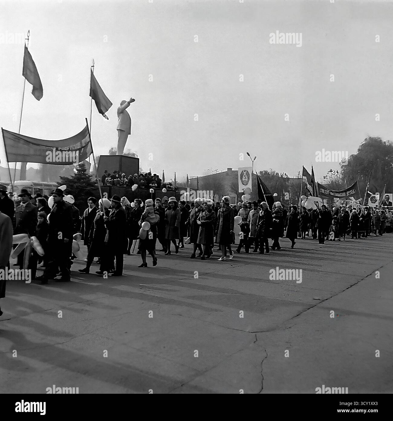 Una suggestiva foto d'archivio del 7 novembre 1974 mostra una parata che celebra l'anniversario della Rivoluzione d'ottobre a Sloviansk. Una lunga colonna di dimostranti, tra cui famiglie e bambini, marcia attraverso la piazza centrale, passando davanti alla monumentale statua di Lenin. I partecipanti portano bandiere, striscioni e ritratti di leader politici. Questa immagine è la quintessenza di una grande festa di stato in URSS, un potente resoconto della vita pubblica collettiva di un pacifico Donba prima della guerra Foto Stock