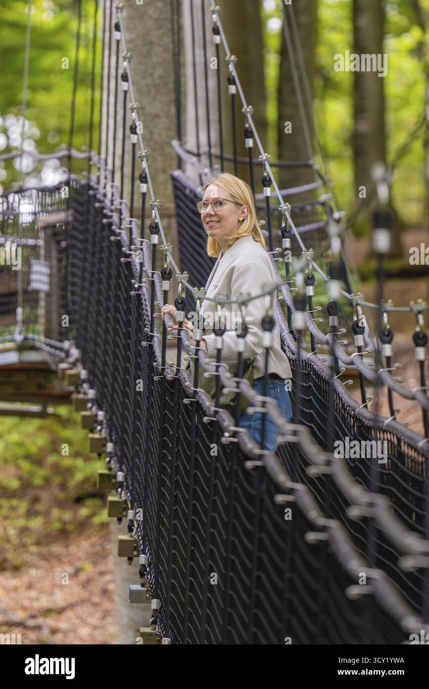 Donna su un ponte di corda attraverso una foresta, Treewalk, Affenberg Salem, Bodenseekreis, Germania Foto Stock