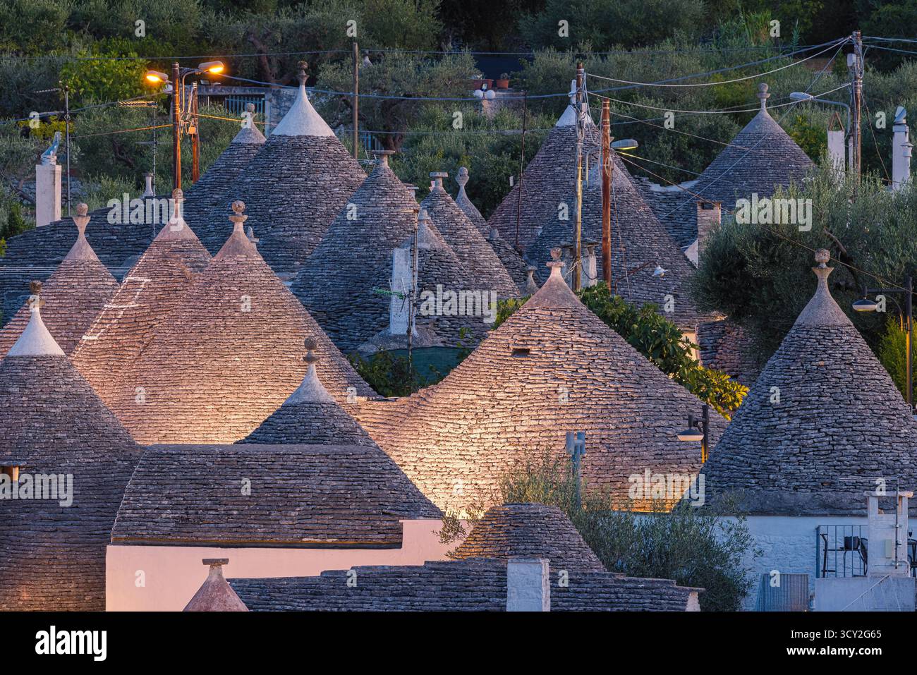 Una splendida scena serale ad Alberobello, in Puglia, in Italia, con le tradizionali case dei Trulli che si illuminano dolcemente di luce calda. I tetti conici e bianchi Foto Stock