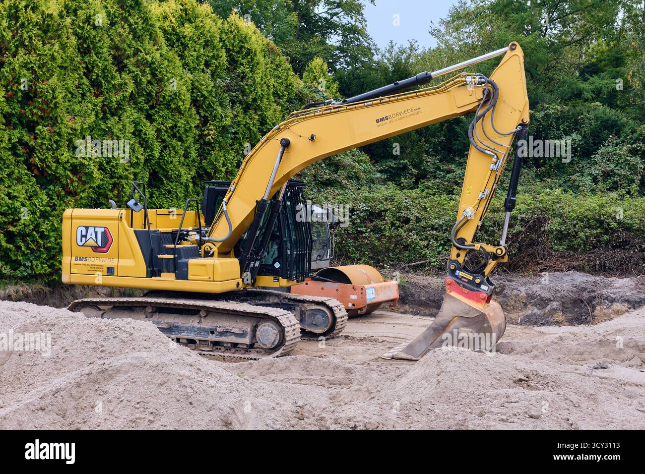 Bassum, Germania; 3 ottobre 2025: L'escavatore giallo Caterpillar e il compattatore a rulli arancioni rimangono inattivi in un cantiere sabbioso a Bassum, Germania, in rea Foto Stock