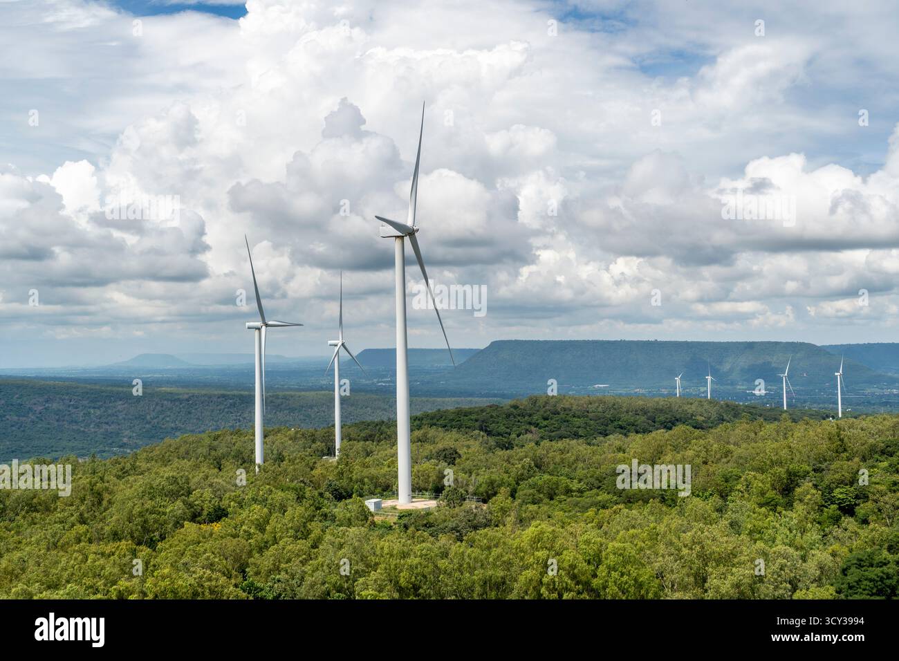La tecnologia energetica sostenibile, che utilizza grandi turbine eoliche, genera energia pulita su una lussureggiante cresta di montagna verde in Asia. La scena, sotto un clou in parte Foto Stock