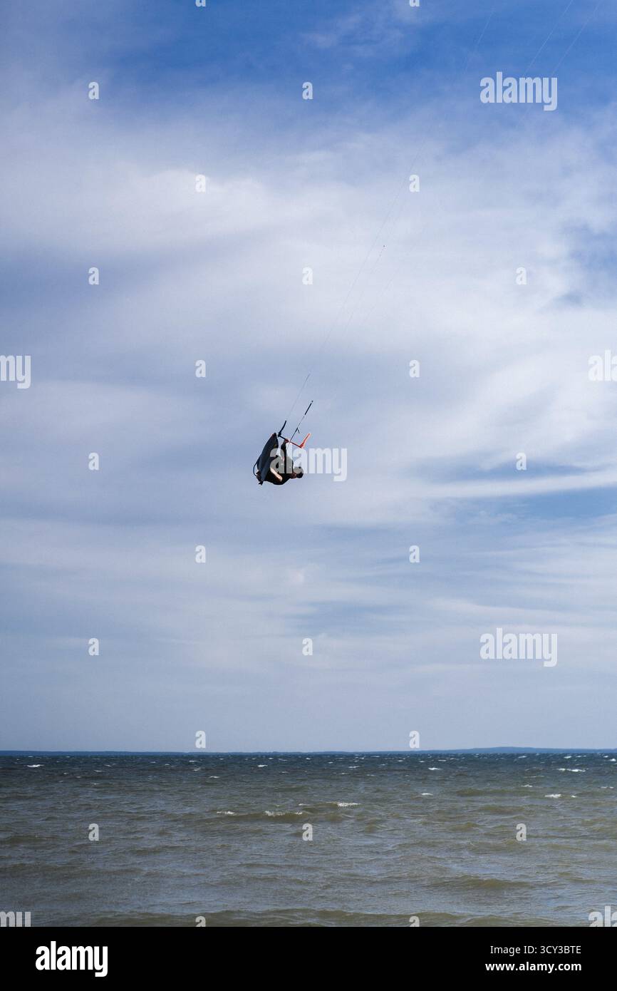 Kiteboarder che esegue un trucco di ribaltamento aereo sopra l'acqua, cielo blu Foto Stock