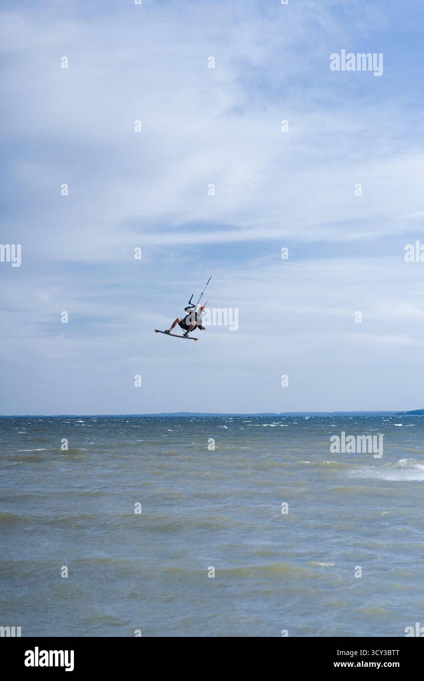 Kiteboarder che esegue un trucco di ribaltamento aereo sopra l'acqua, cielo blu Foto Stock