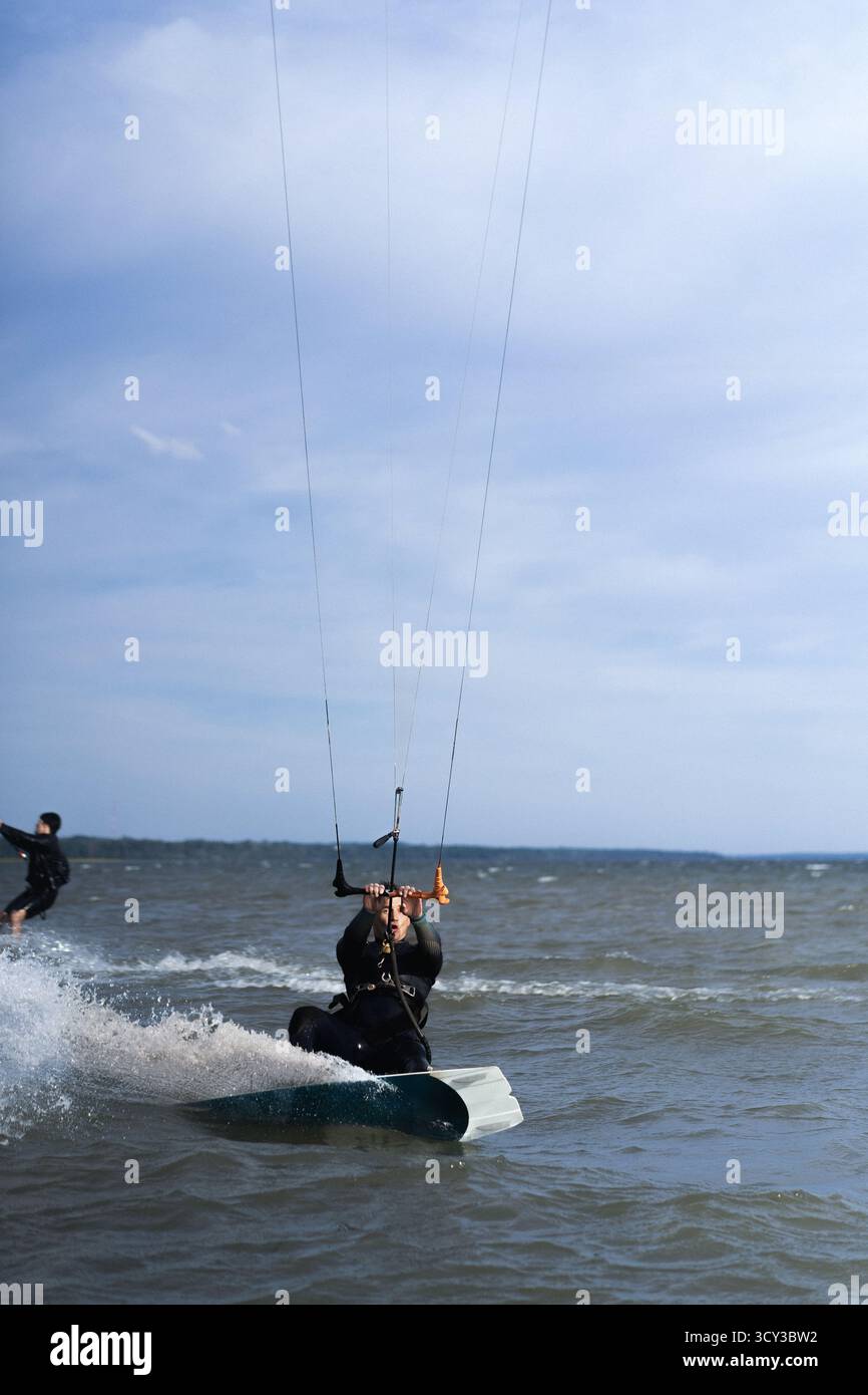 Kitesurfer in muta che scivola attraverso l'acqua instabile in una giornata di sole Foto Stock