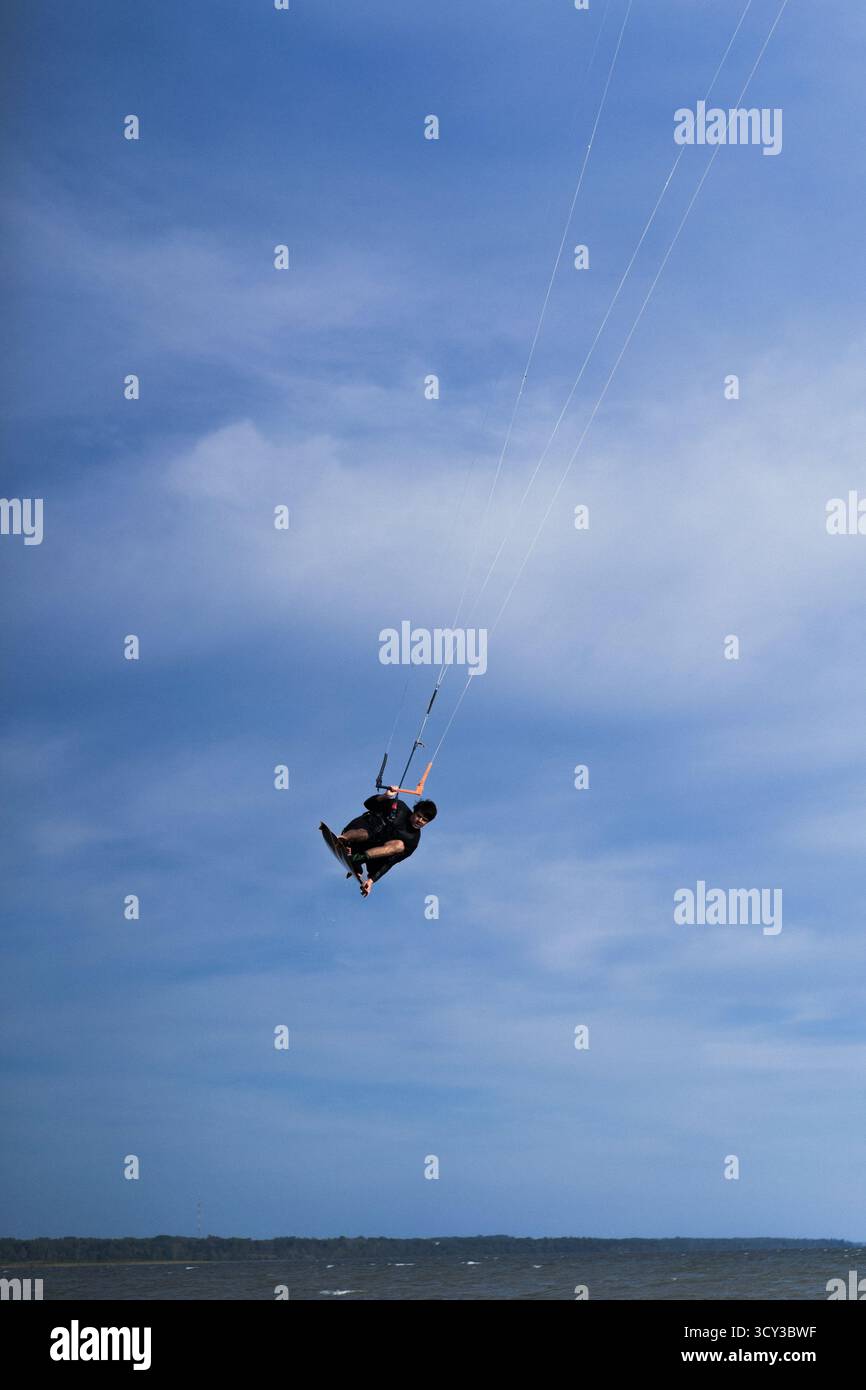 Kiteboarder che esegue un trucco di ribaltamento aereo sopra l'acqua, cielo blu Foto Stock