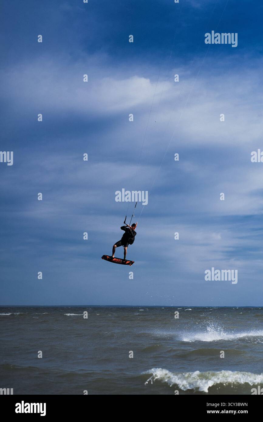 Kiteboarder che esegue un trucco di ribaltamento aereo sopra l'acqua, cielo blu Foto Stock