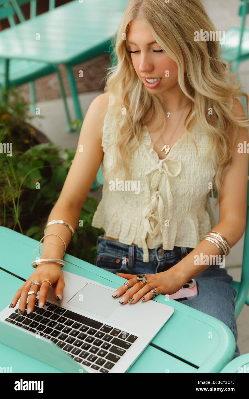Una giovane donna sceglie un computer portatile in un colorato caffè all'aperto Foto Stock