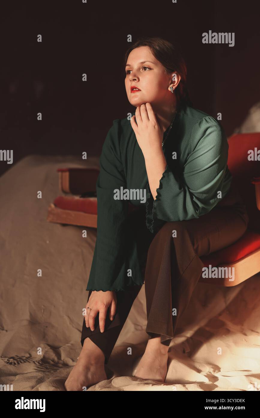 Donna in camicetta verde che posa con cura su una sedia rossa Foto Stock