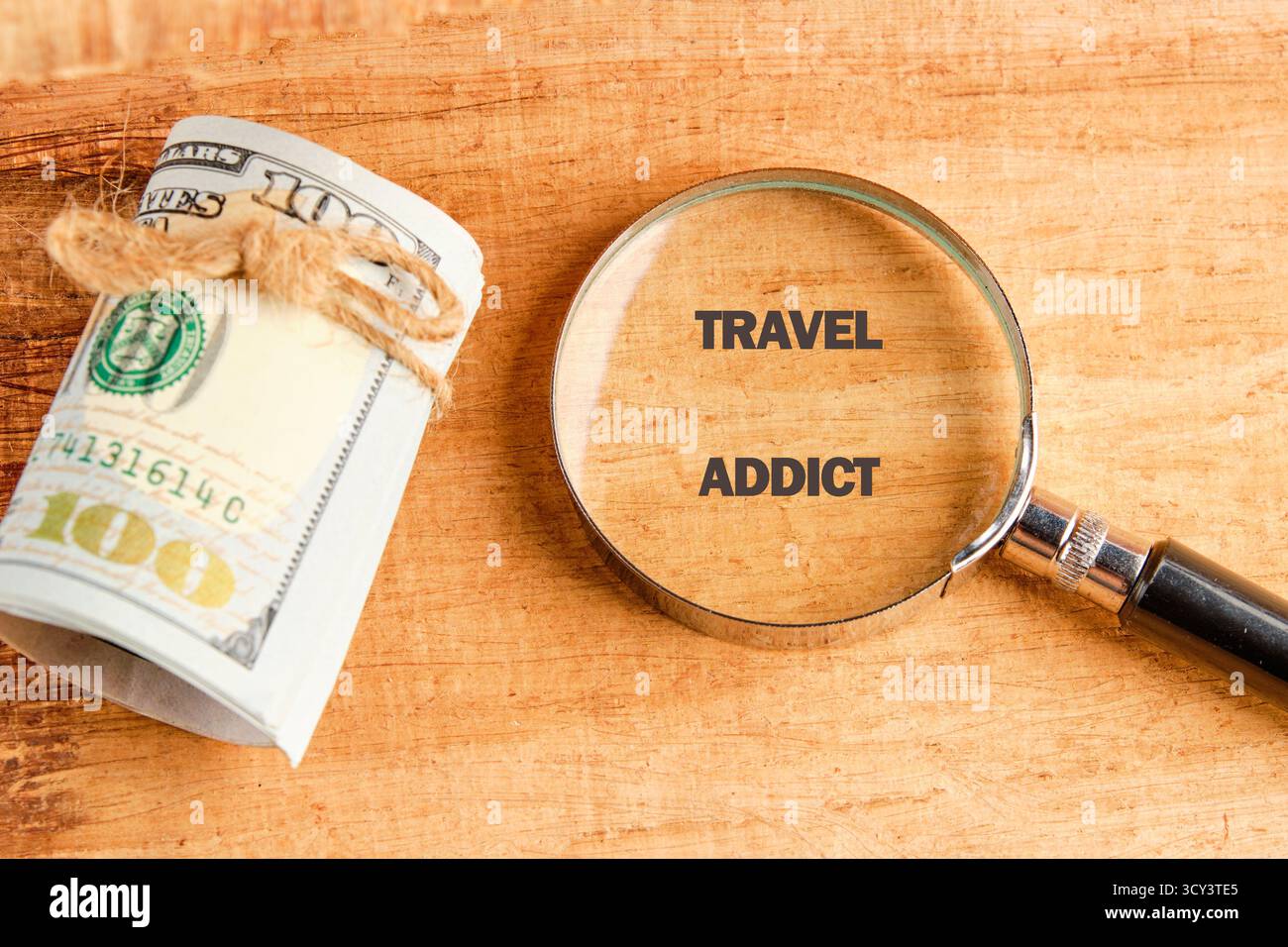 Accanto a una lente d'ingrandimento si trova un mazzo di contanti che sottolinea le parole "dipendente dai viaggi". La scena cattura l'emozione di pianificare nuovi progetti Foto Stock