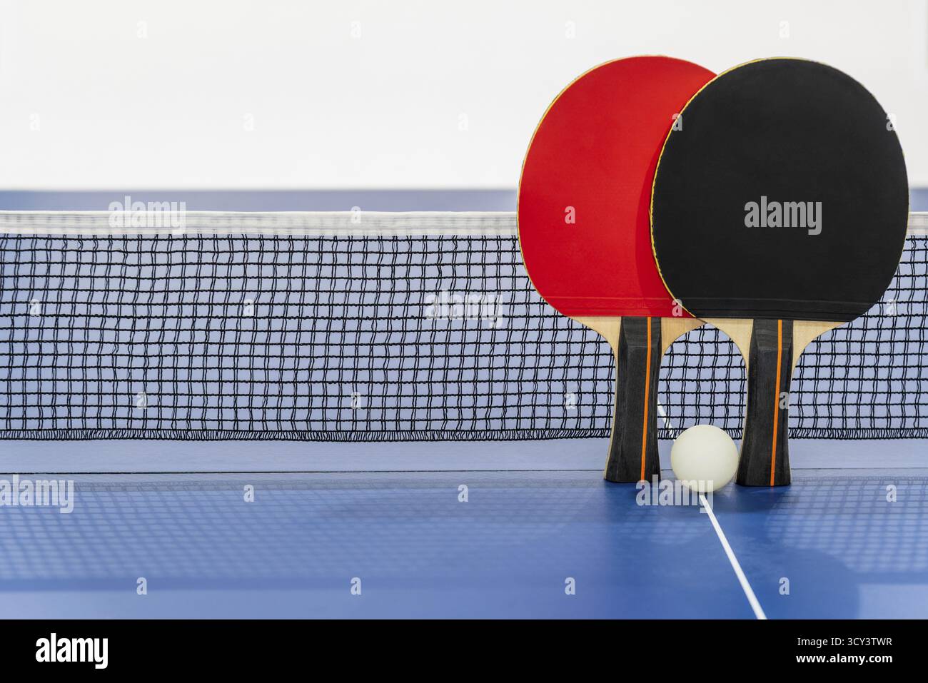 Racchetta da ping pong nera e rossa e una palla bianca sul tavolo da ping pong blu con rete, due paddle da ping pong è un'attrezzatura sportiva da competizione i Foto Stock