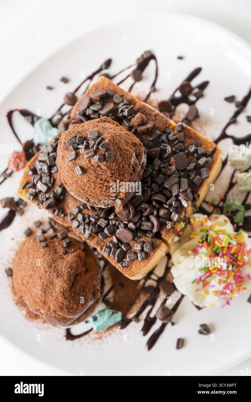 Primo piano vista dall'alto pane al Miele e paletta per gelato al cioccolato con sciroppo decorare con una pastiglia di cioccolato in un piatto bianco sul tavolo Foto Stock