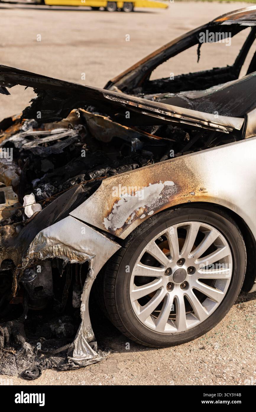 Un'auto con gravi danni da incendio è parcheggiata in un sacco. L'interno carbonizzato rivela le conseguenze di un incendio, mostrando parti fuse e un esterno rovinato Foto Stock