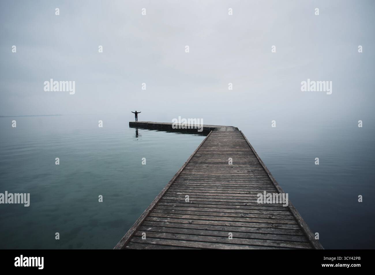 Uomo con le braccia alzate contro la luce alla fine di un molo sul mare alla luce della sera Foto Stock